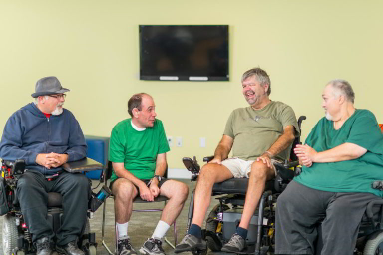 Four men is wheel chairs in a group-style meeting