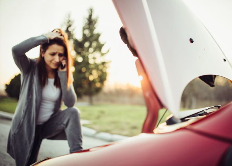 Woman with a broken down car on the side of the road making a call